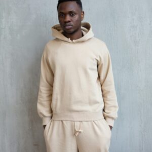 Confident young African American guy in white hoodie and pants standing in light studio on white background and looking at camera